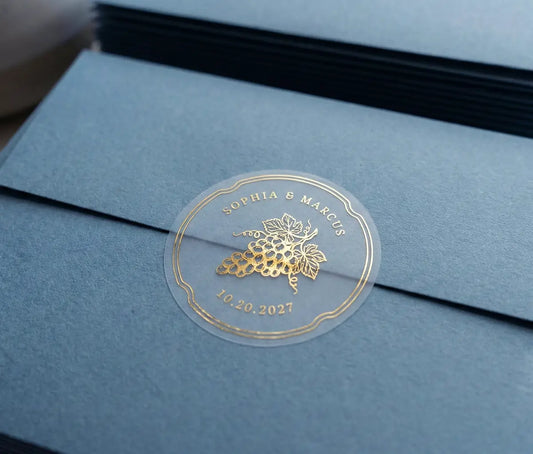 Vineyard theme wedding envelope stickers with custom names and date printed in gold foil and used to seal slate blue envelope.
