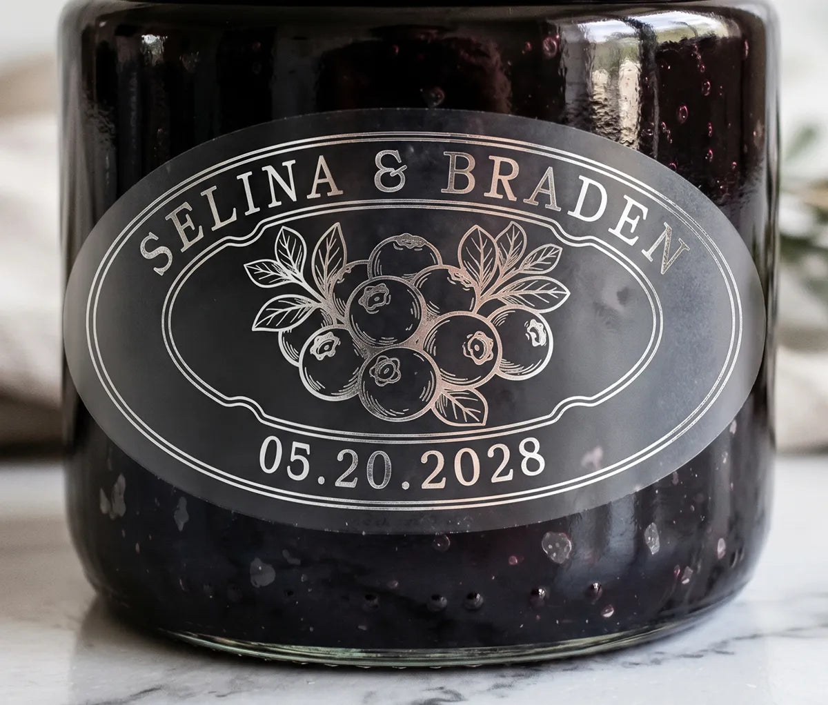 Oval personalized silver foil print frosted wedding favour label on a blueberry jam jar.