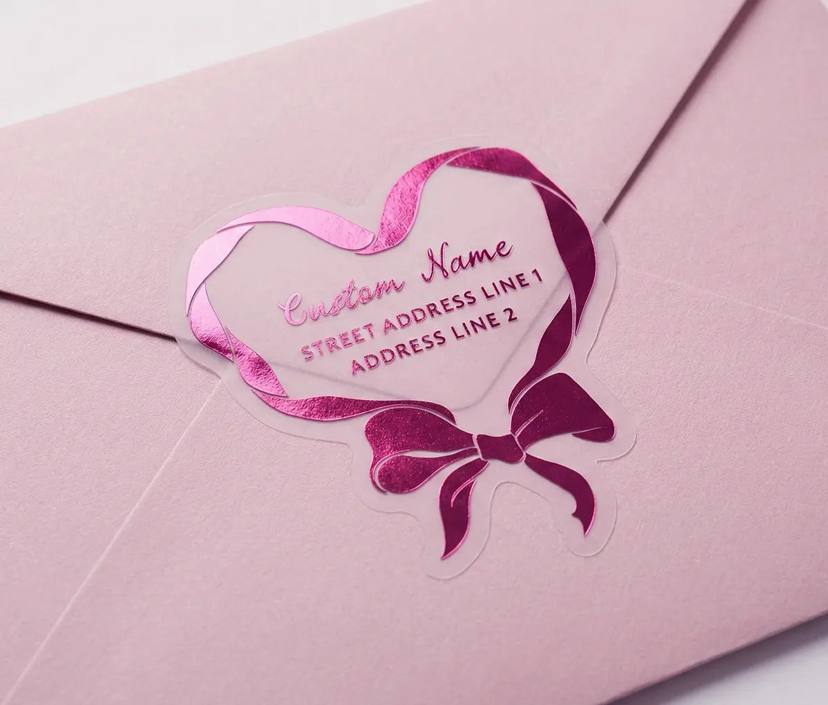 Ribbon in heart shape return address labels printed in hot pink foil on transparent frosted vinyl sealing an envelope