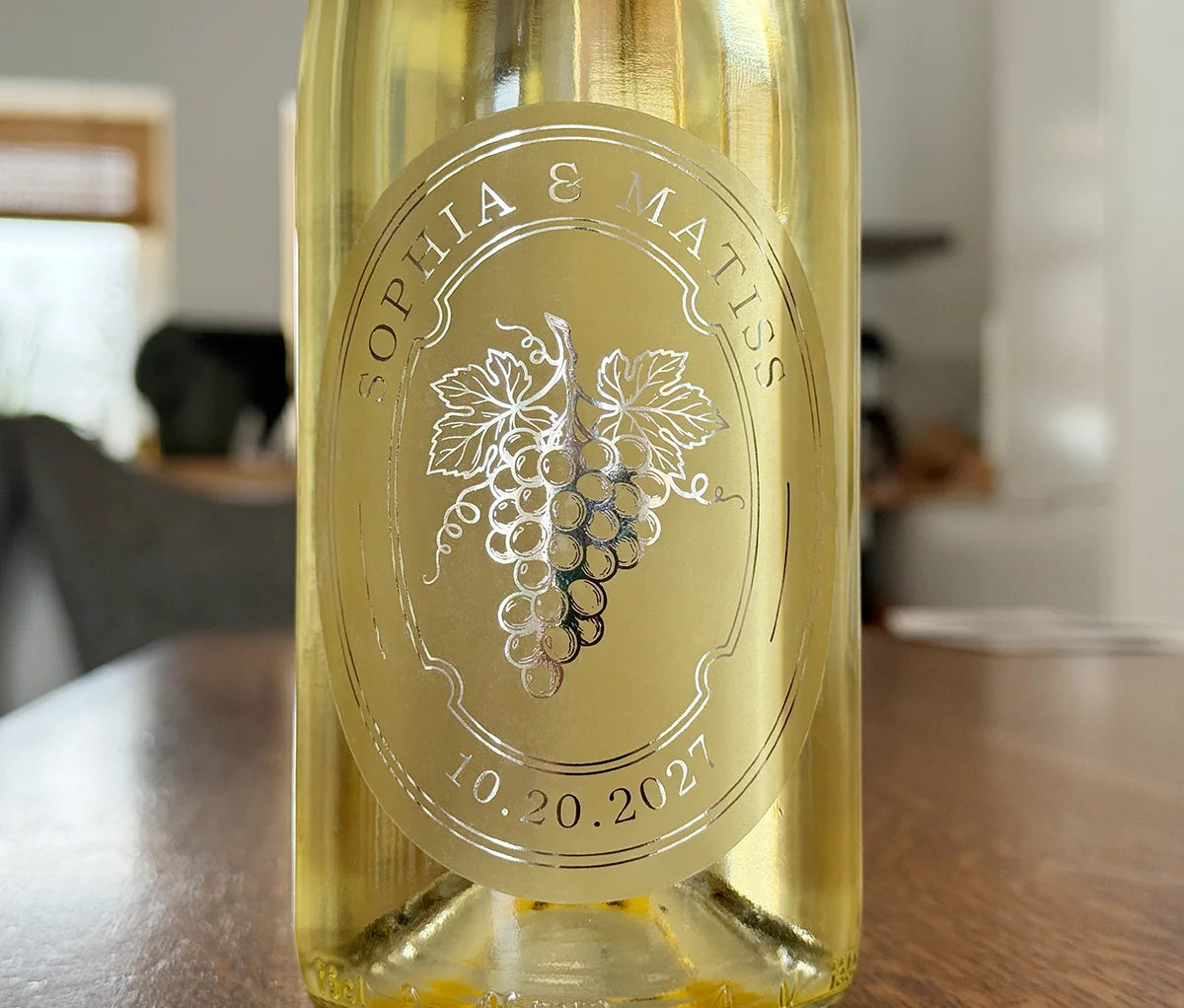 White wine bottle with an oval personalized frosted label featuring grapes printed in silver foil.