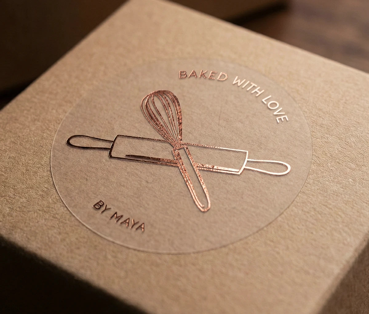 'Baked with Love' personalized sticker printed in rose gold foil applied to a kraft box.