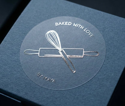 Small blue box with silver foil printed sticker with an imagage of a whisk and rolling pin, and text 'Baked with Love by Maya'