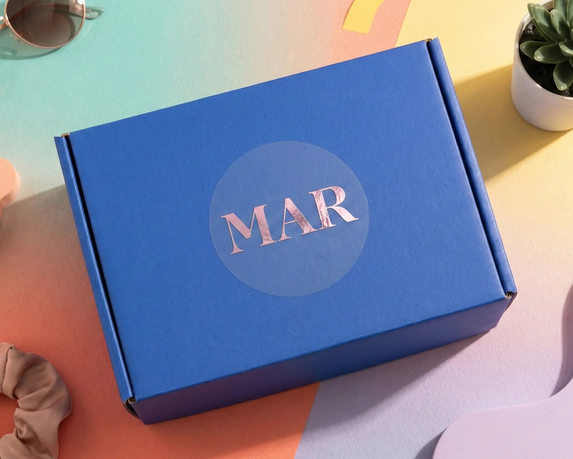 Colourful, vibrant background and blue box with custom logo sticker printed in pale pink foil on clear matte vinyl.
