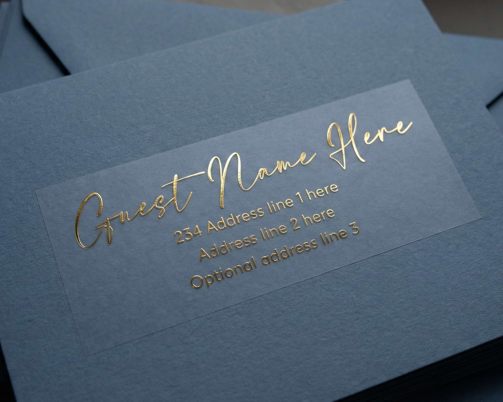 Custom Guest Address Label printed in calligraphy font and in gold foil on transparent matte sticker and applied to a slate blue envelope.