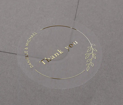 Wedding thank you sticker with personalized names and delicate floral theme frame printed in gold on clear sticker