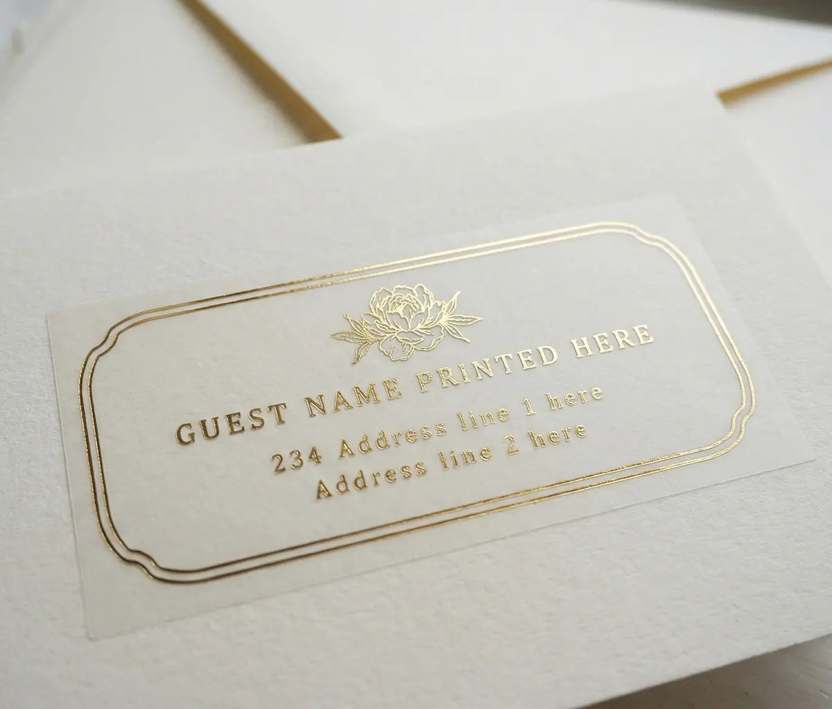 White envelope with luxurious floral recipient address label with peony graphic printed in gold foil on transparent vinyl.