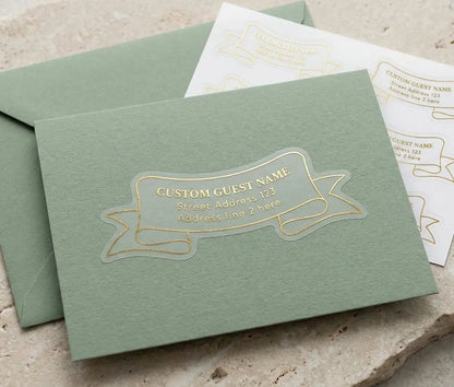 Recipient address label printed in gold foil and custom cut in ribbon shape applied to the front of a sage envelope.