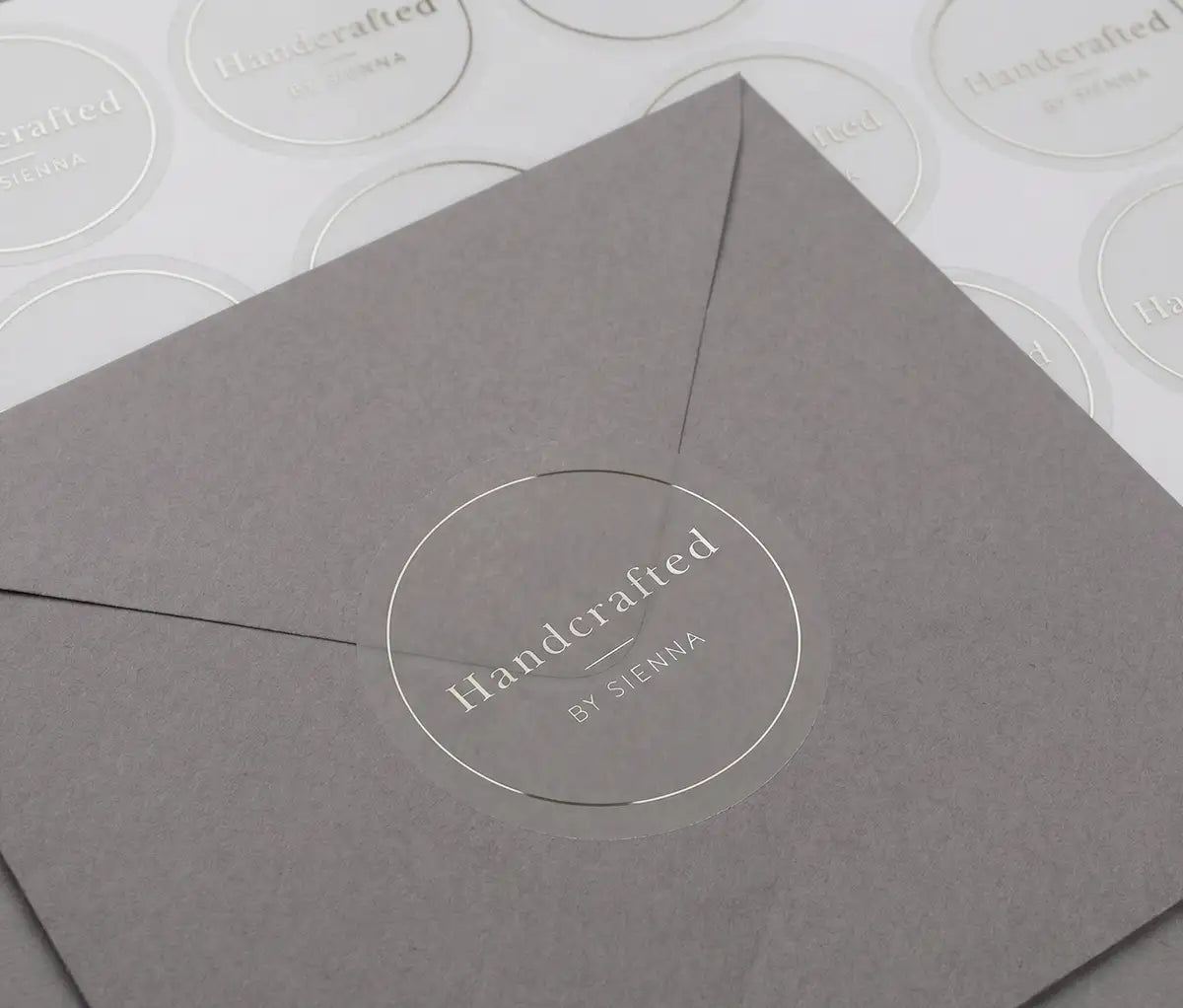 "Handcrafted" business sticker is printed in silver foil and applied to a grey envelope. There is a sticker sheet behind the envelope.