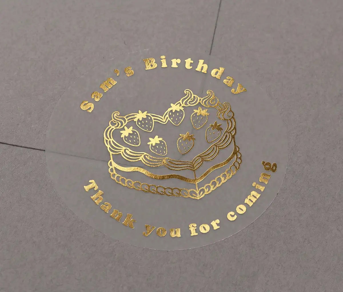 Heart shaped birthday cake, custom name and text "Thank you for coming" printed in gold on transparent sticker that is applied to a grey envelope.