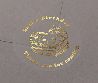 Heart shaped birthday cake, custom name and text "Thank you for coming" printed in gold on transparent sticker that is applied to a grey envelope.