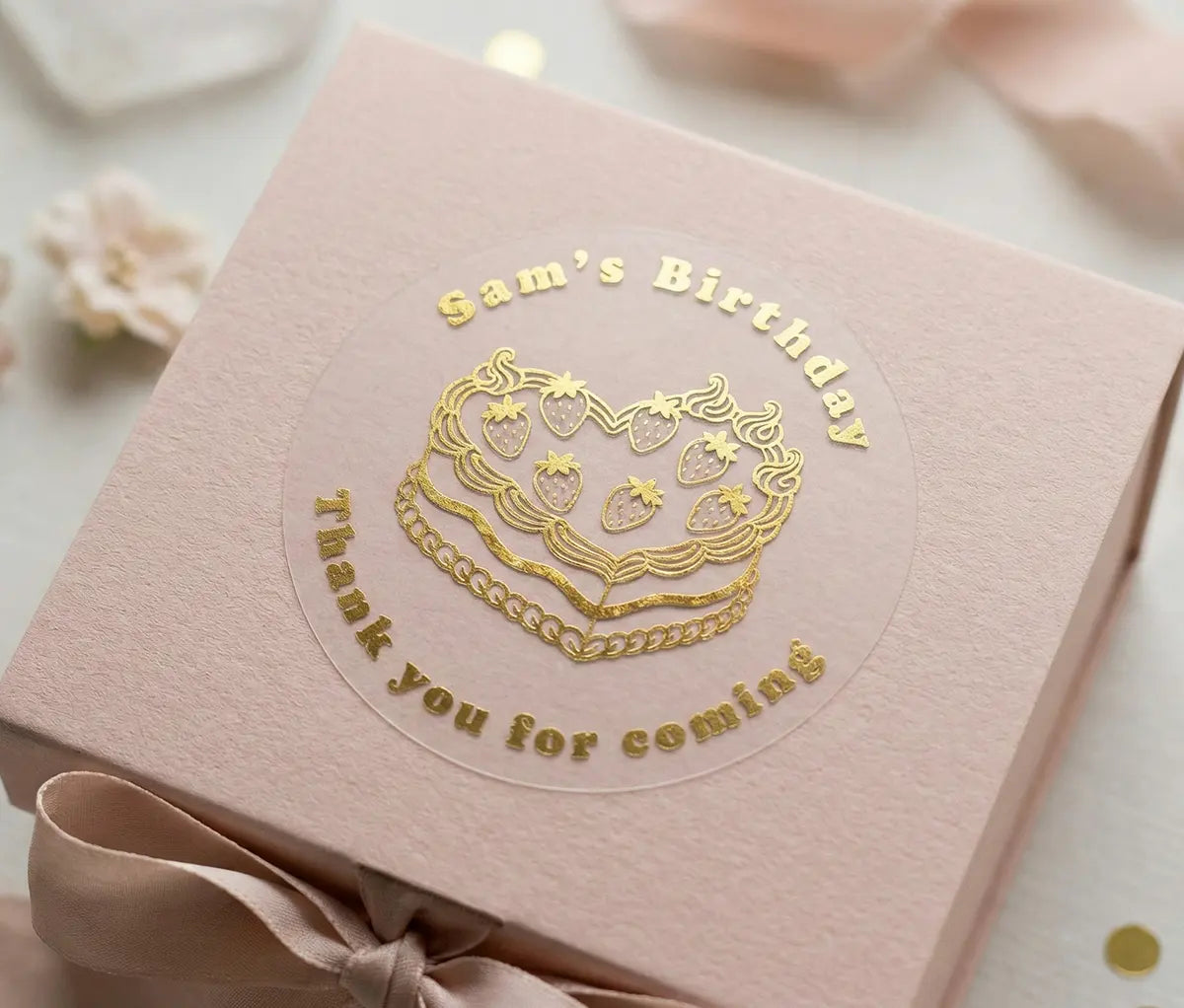 Personalised birthday sticker applied to a lid of a pink gift box. Custom name, text "Thank you for coming" and heart shaped cake is printed in gold foil on frosted sticker.