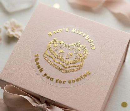 Personalised birthday sticker applied to a lid of a pink gift box. Custom name, text "Thank you for coming" and heart shaped cake is printed in gold foil on frosted sticker.