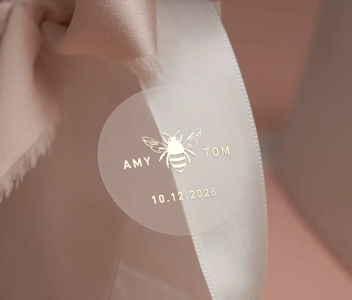 Honey bee graphic and personalized names printed in gold on round clear sticker and applied to a white ribbon