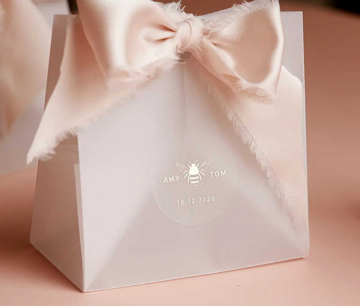 Honey bee graphic and personalized names printed in gold on round clear sticker and applied to a favor packaging
