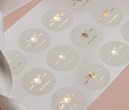 Sticker sheet of Honey bee graphic and personalized names printed and date printed in gold foil on round clear stickers.