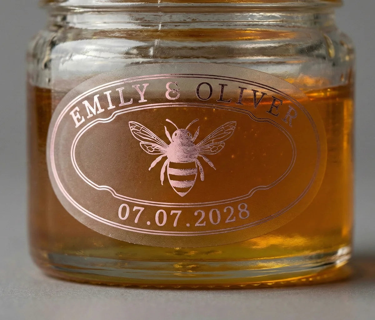 Jar of honey with a personalized oval shape label featuring a bee printed in pale pink foil on frosted vinyl.
