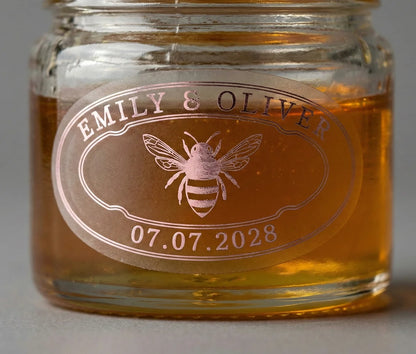 Jar of honey with a personalized oval shape label featuring a bee printed in pale pink foil on frosted vinyl.