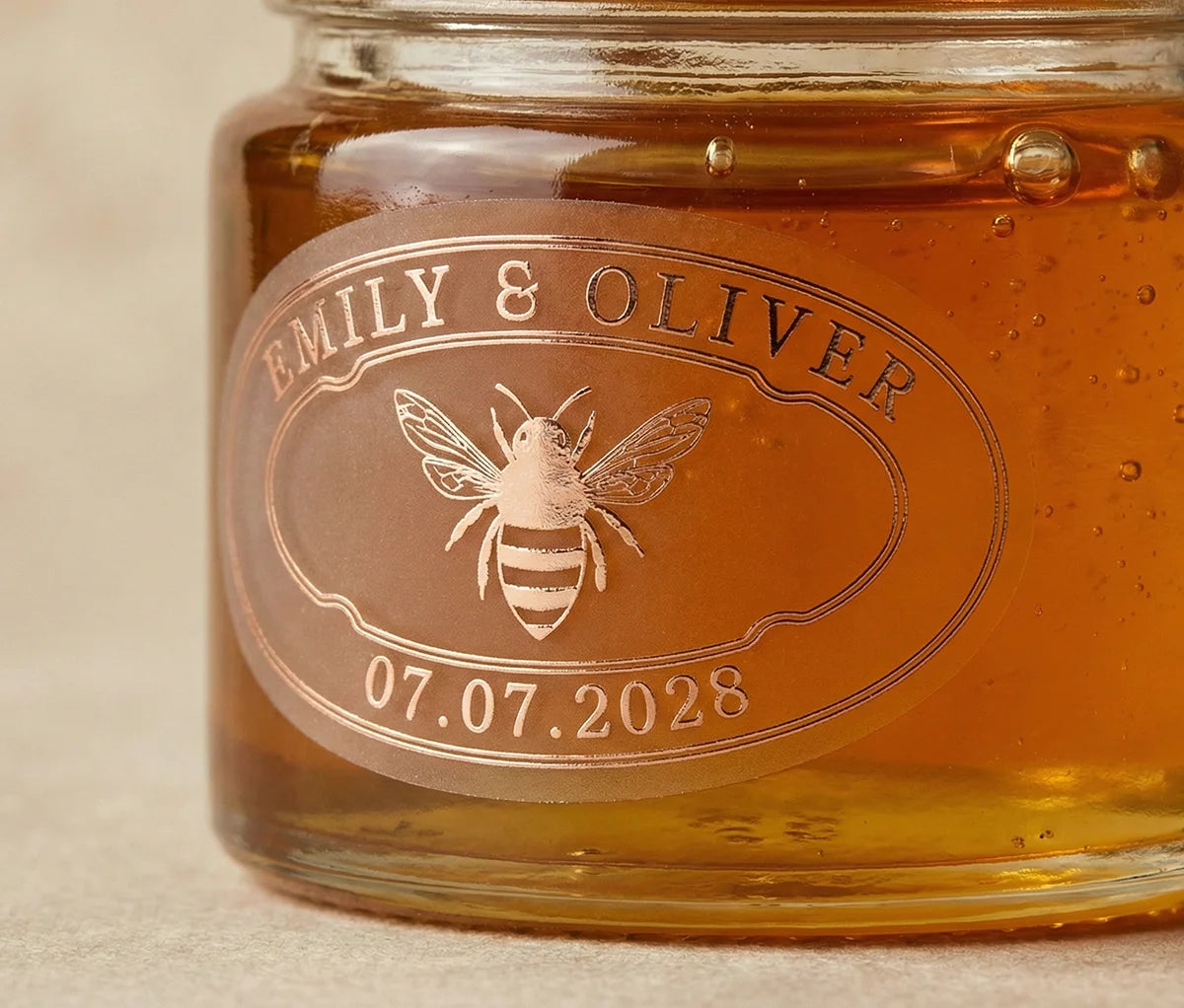 Jar of honey with personalized oval wedding favour label printed in rose gold foil on frosted vinyl.