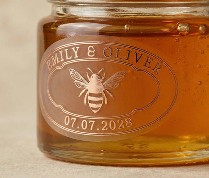 Jar of honey with personalized oval wedding favour label printed in rose gold foil on frosted vinyl.