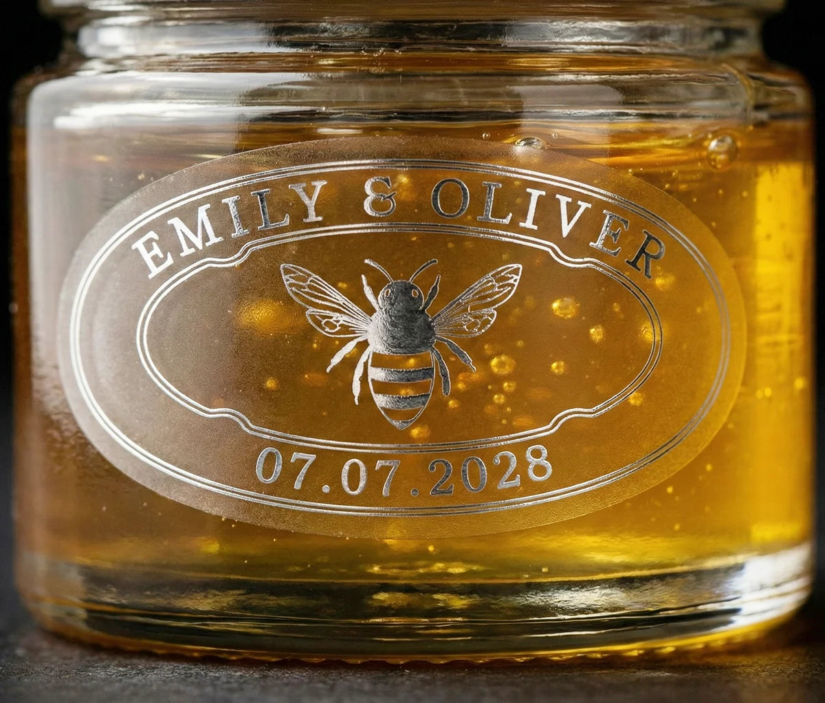 Jar of honey with personalized oval wedding favour label printed in silver foil on frosted vinyl.
