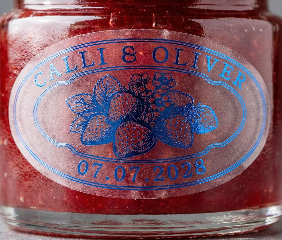 Jar of strawberry jam with personalized oval shape wedding favor sticker printed in royal blue foil on frosted vinyl.