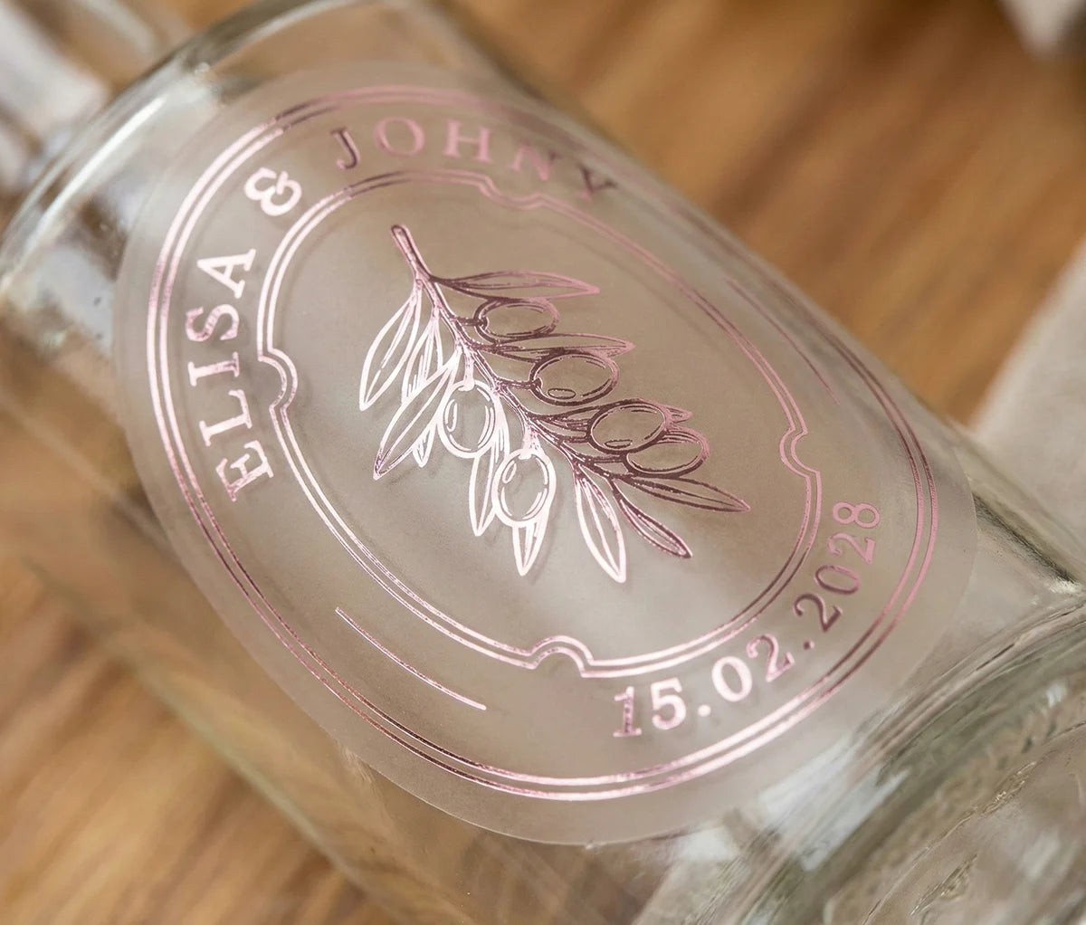 Glass bottle with personalized oval frosted sticker featuring olive graphic printed in pale pink foil.