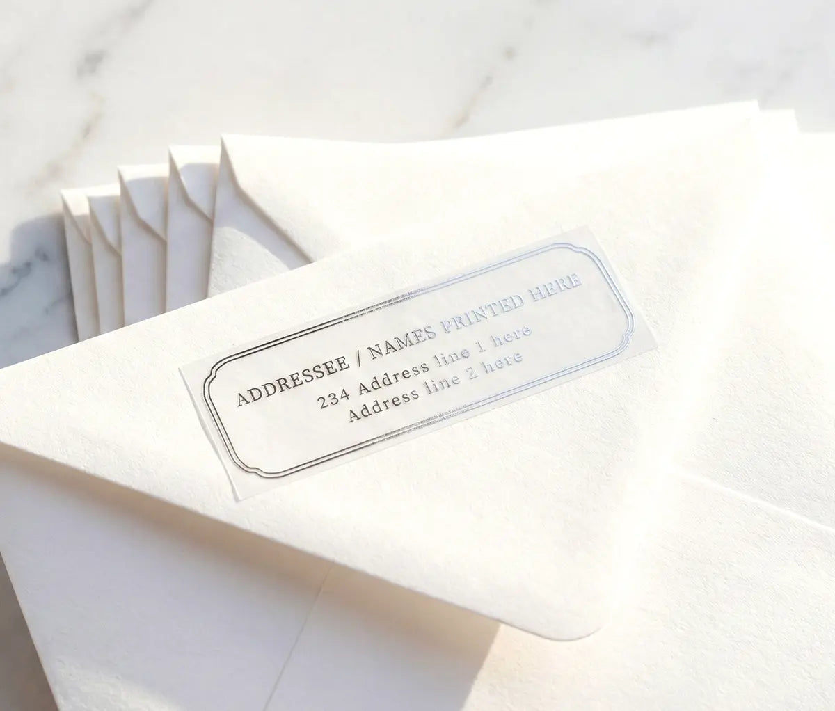 White envelope with luxurious return address label printed in silver foil on transparent vinyl.