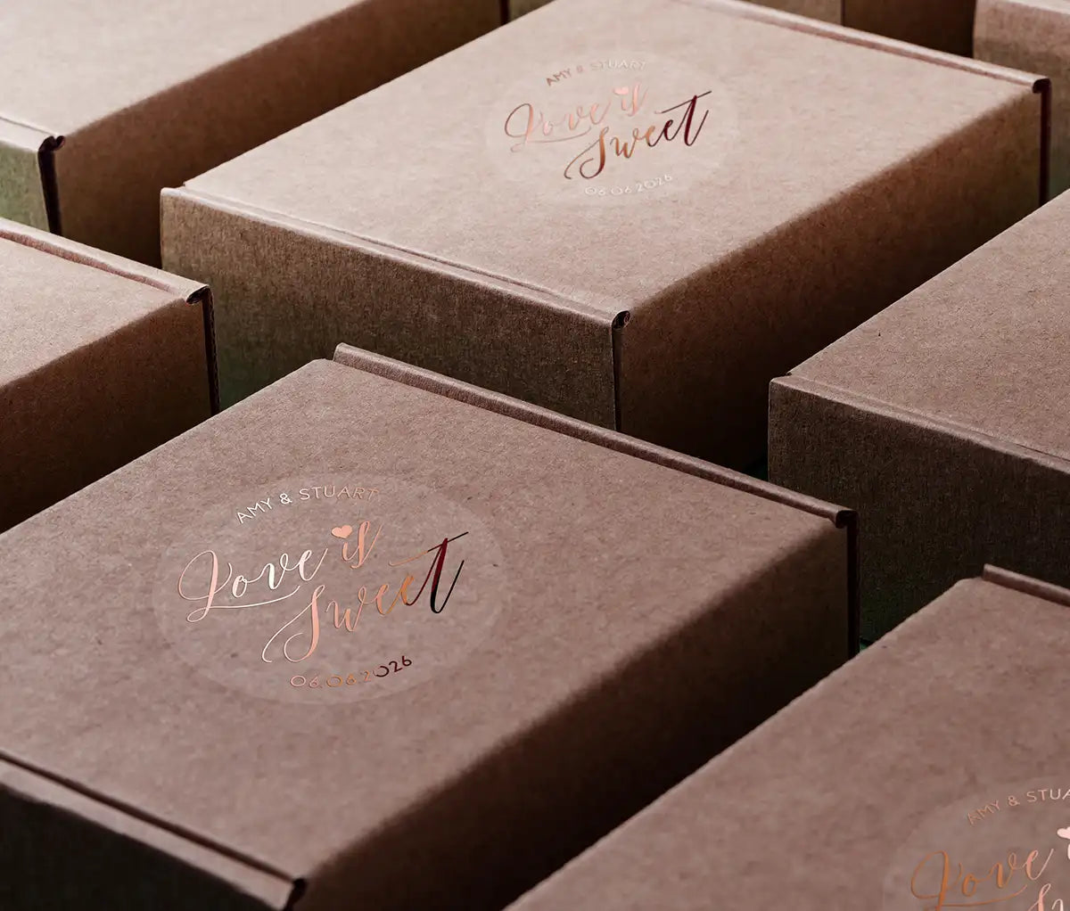 Love is sweet wedding favor sticker with heart graphic personalized names and date printed in rose gold and applied to boxes