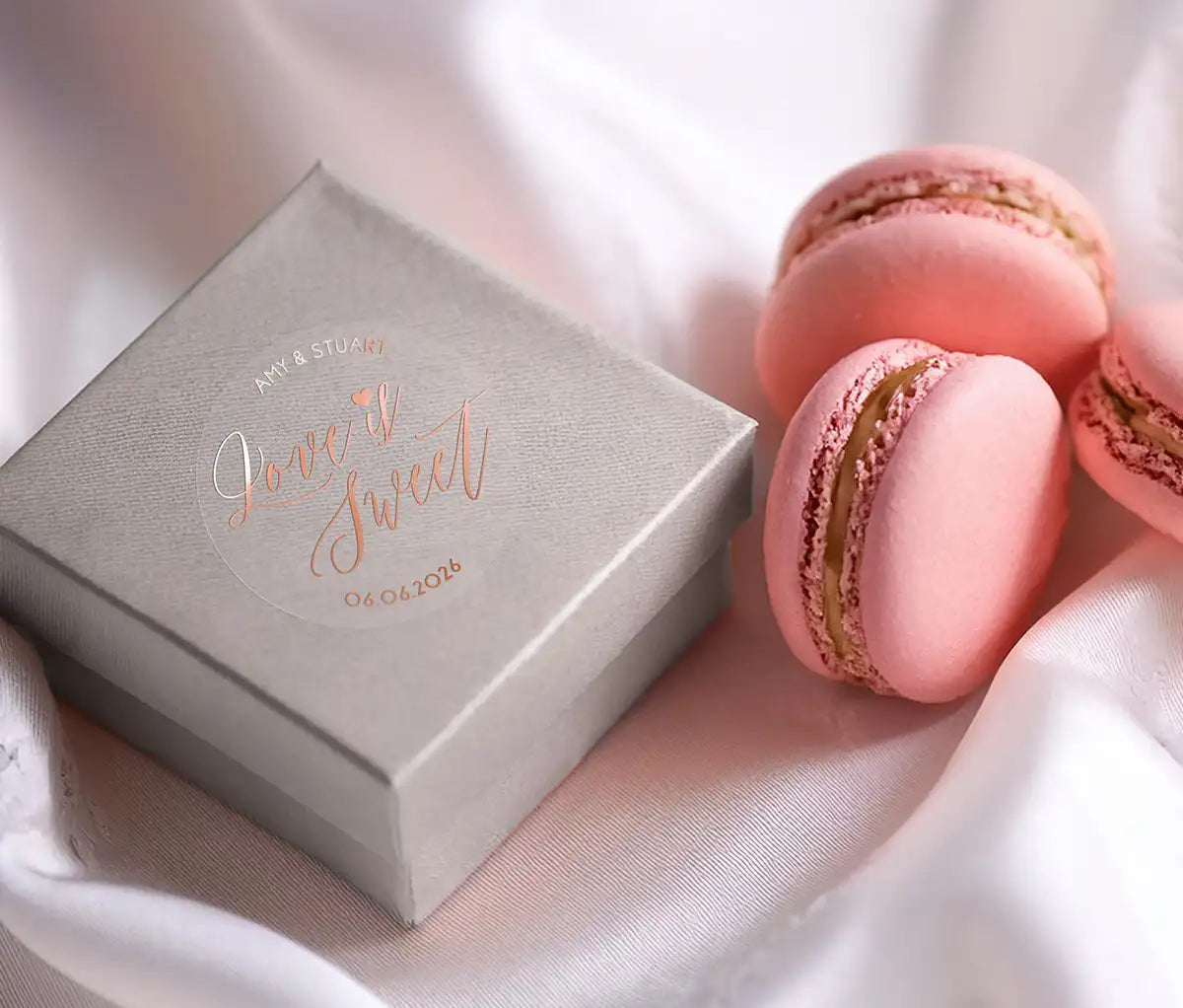 Love is sweet wedding favor sticker with heart graphic personalized names and date printed in rose gold and applied to a small box