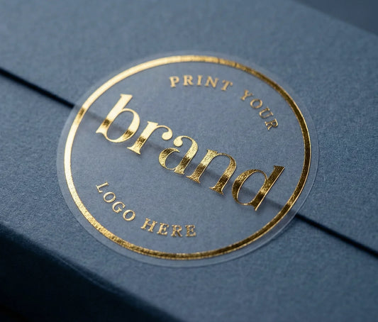 Custom, round, transparent matte logo sticker printed in real gold foil, creating a luxury frosted look on a navy blue product box.