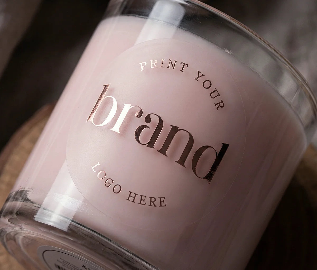 Round, clear matte logo sticker printed in rose gold foil applied to a glass candle container, demonstrating a premium frosted glass effect.
