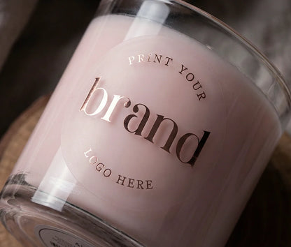 Round, clear matte logo sticker printed in rose gold foil applied to a glass candle container, demonstrating a premium frosted glass effect.