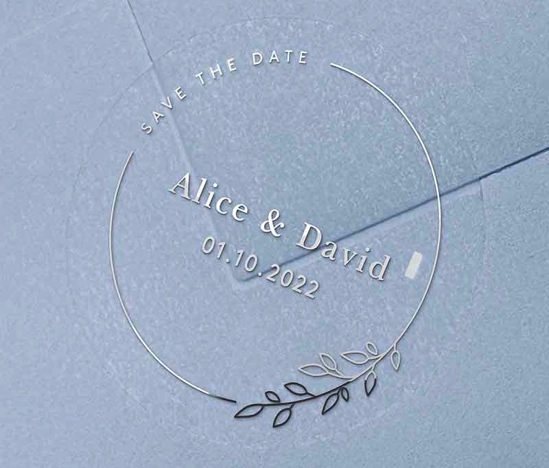 Save The Date sticker with personalised names and date and thin frame with leaves printed in silver on clear round label