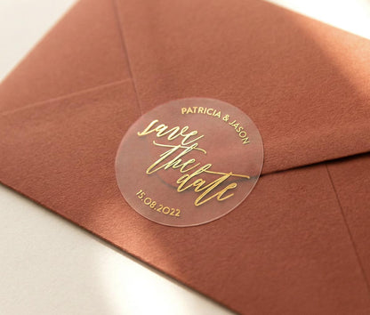Brown envelope with a clear 'save the date' sticker featuring custom names and date printed in gold foil.