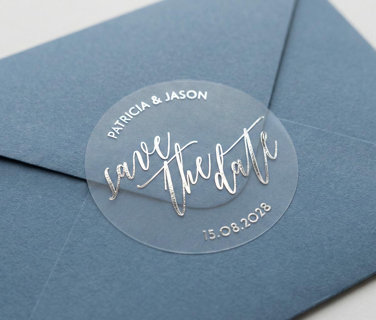 Navy blue envelope with a clear 'save the date' sticker featuring custom names and date printed in silver foil.