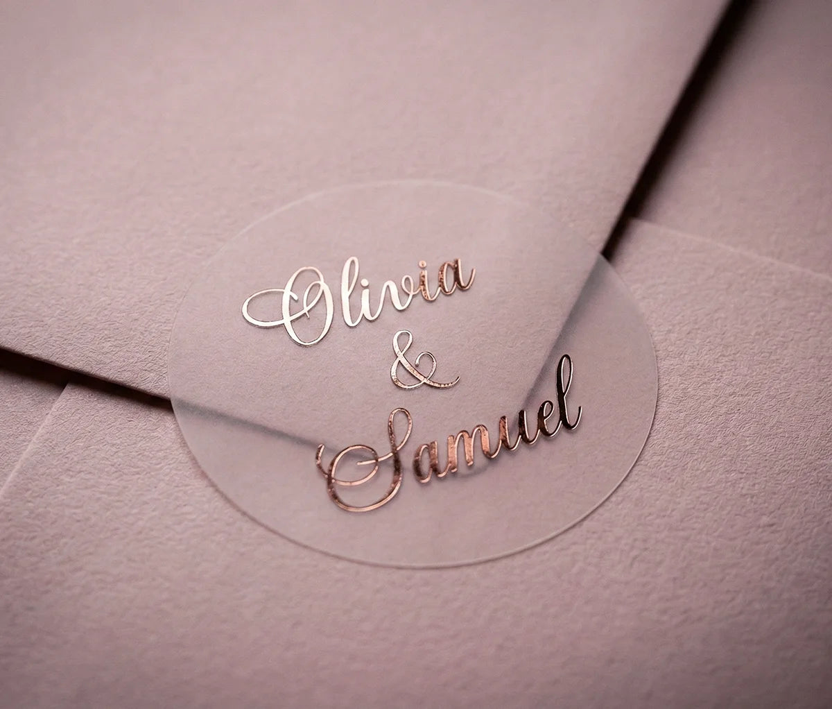 Round clear label with custom names printed in rose gold applied to a dusty pink envelope.