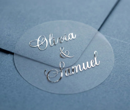 Round transparent wedding sticker with custom names printed in silver foil applied to navy colour envelope.