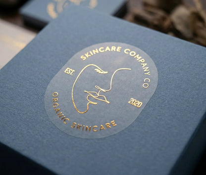 Skincare brand sticker with personalized text on oval frosted sticker printed in Gold Foil and applied to slate blue box.