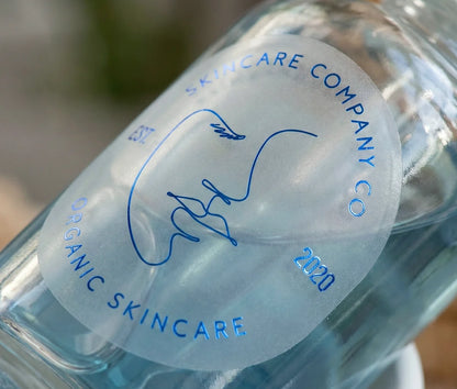 Skincare brand sticker with customizable text on oval frosted sticker printed in Royal Blue Foil and applied to a blue skincare serum bottle.