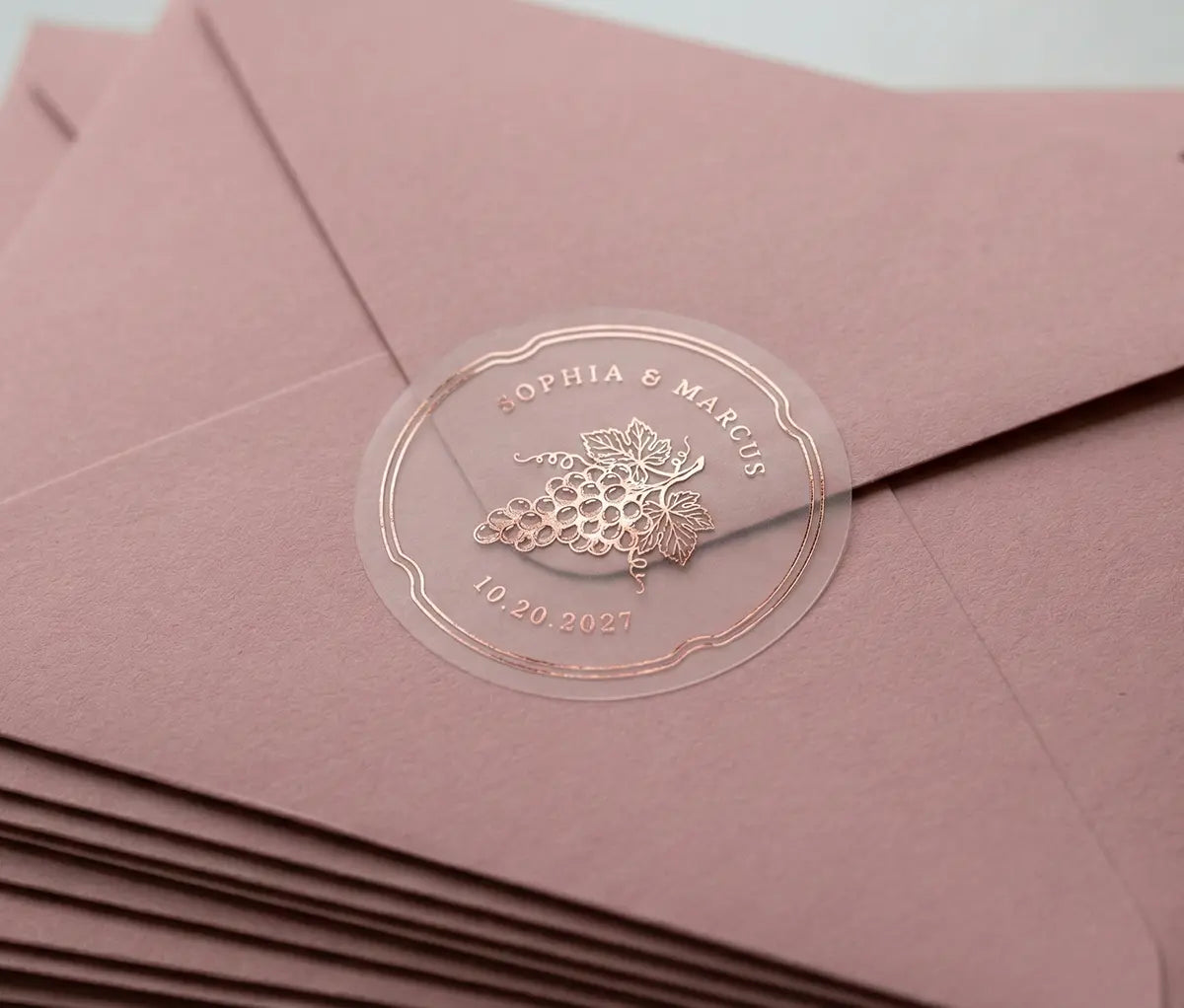 Vineyard theme wedding envelope stickers with custom names and date printed in rose gold foil and used to seal pink envelope.