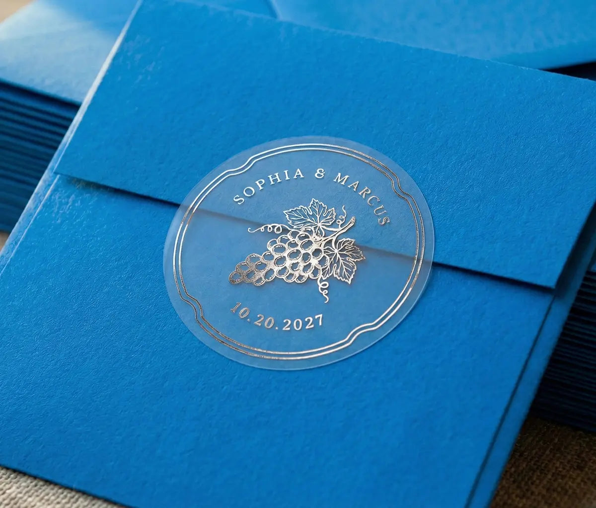 Vineyard theme wedding envelope stickers with custom names and date printed in silver foil and used to seal blue envelope.