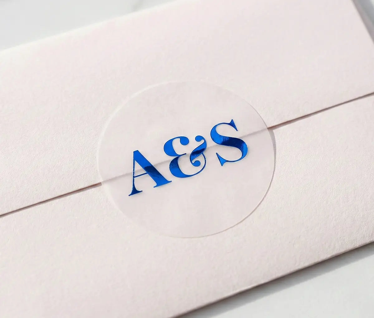 Pale Pink envelope with round Wedding envelope seal with custom initials printed in Royal Blue foil on transparent matte vinyl.