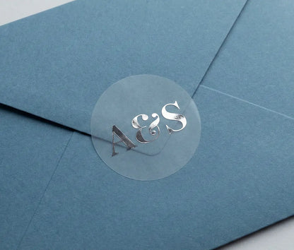 Blue envelope with round Wedding envelope stisker with personalized initials printed in silver foil on transparent matte vinyl.