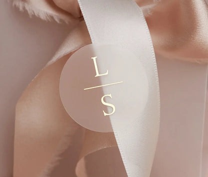 Personalized initials printed in gold foil on round clear sticker and applied to a wedding favour