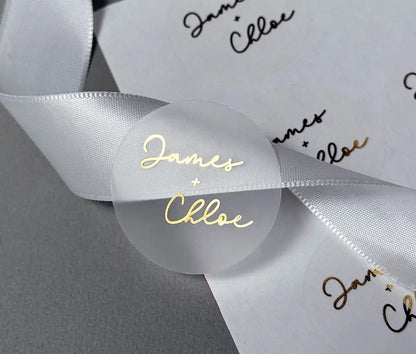 Personalized names in script font and plus sign printed in gold on clear wedding envelope sticker