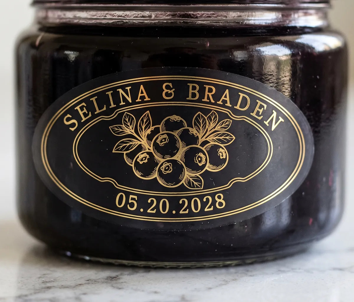 Oval personalized gold foil print matte wedding favour label on a blueberry jam jar.