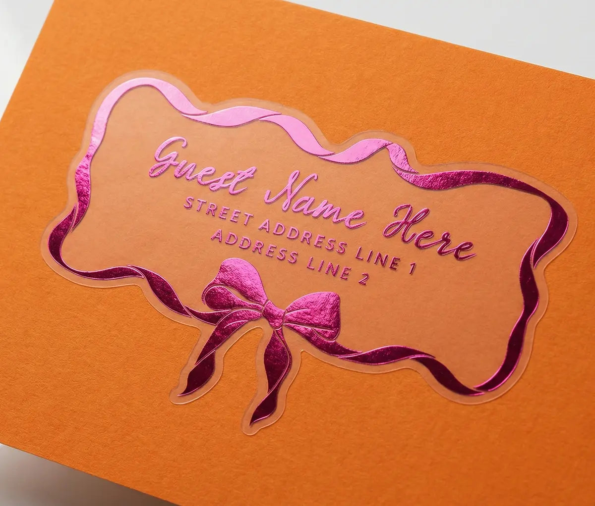 Guest address label printed in hot pink foil applied to orange colour envelope with custom die-cut coquette bow and ribbon shape.