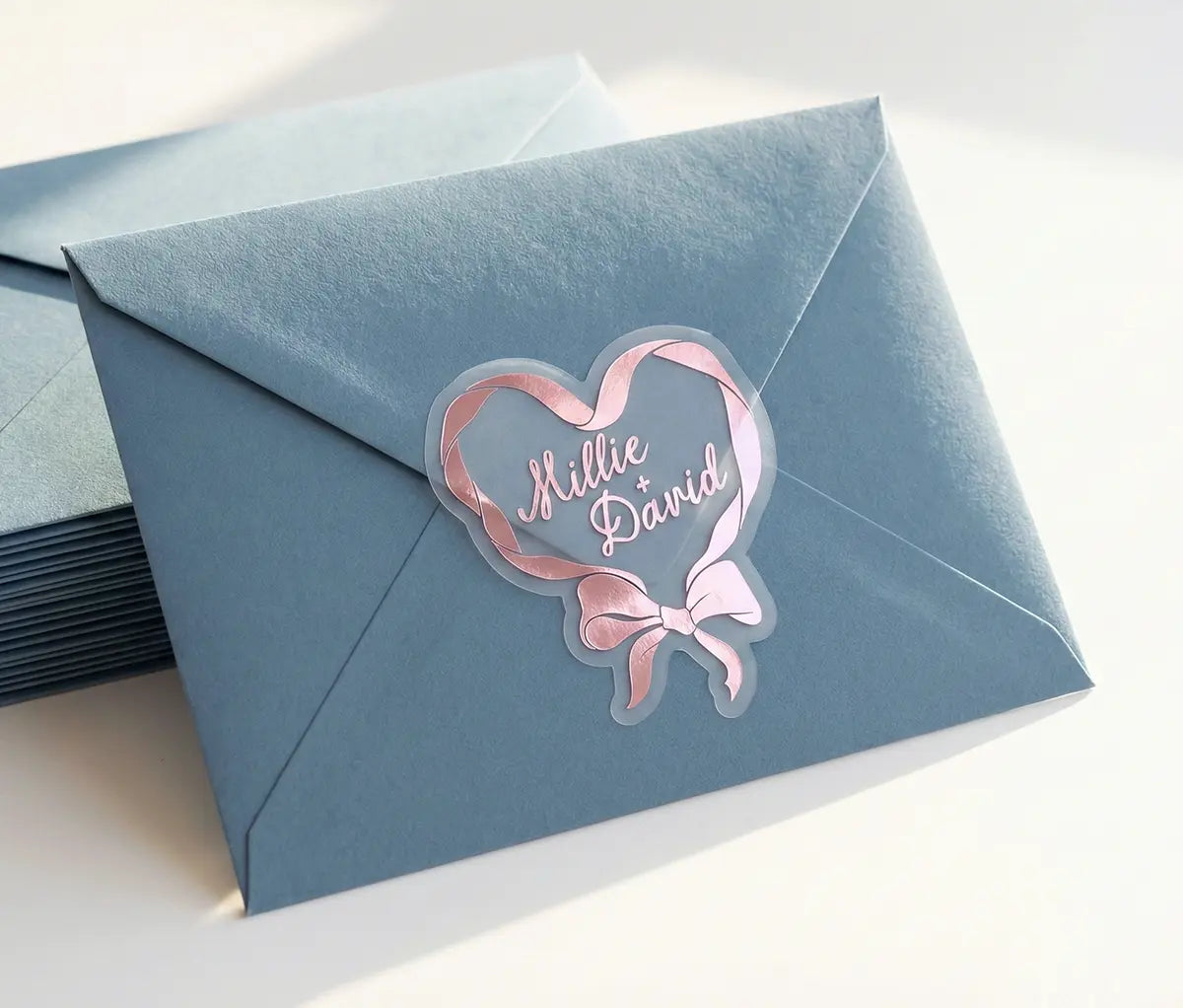Pink foil heart-shaped wedding sticker with custom names sealing blue envelope