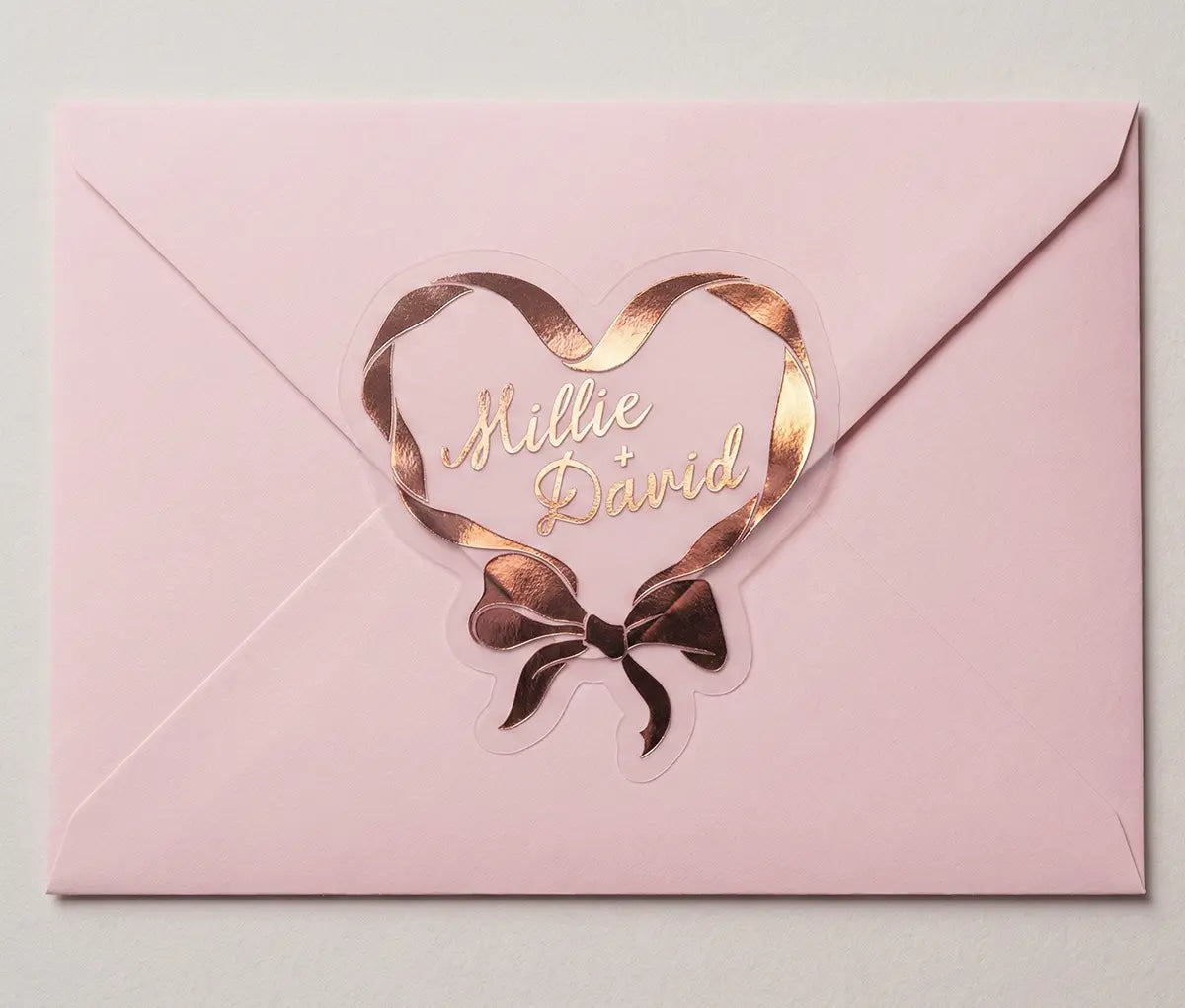 Ribbon in heart shape wedding labels with couples names printed in rose gold foil on transparent frosted vinyl sealing an envelope