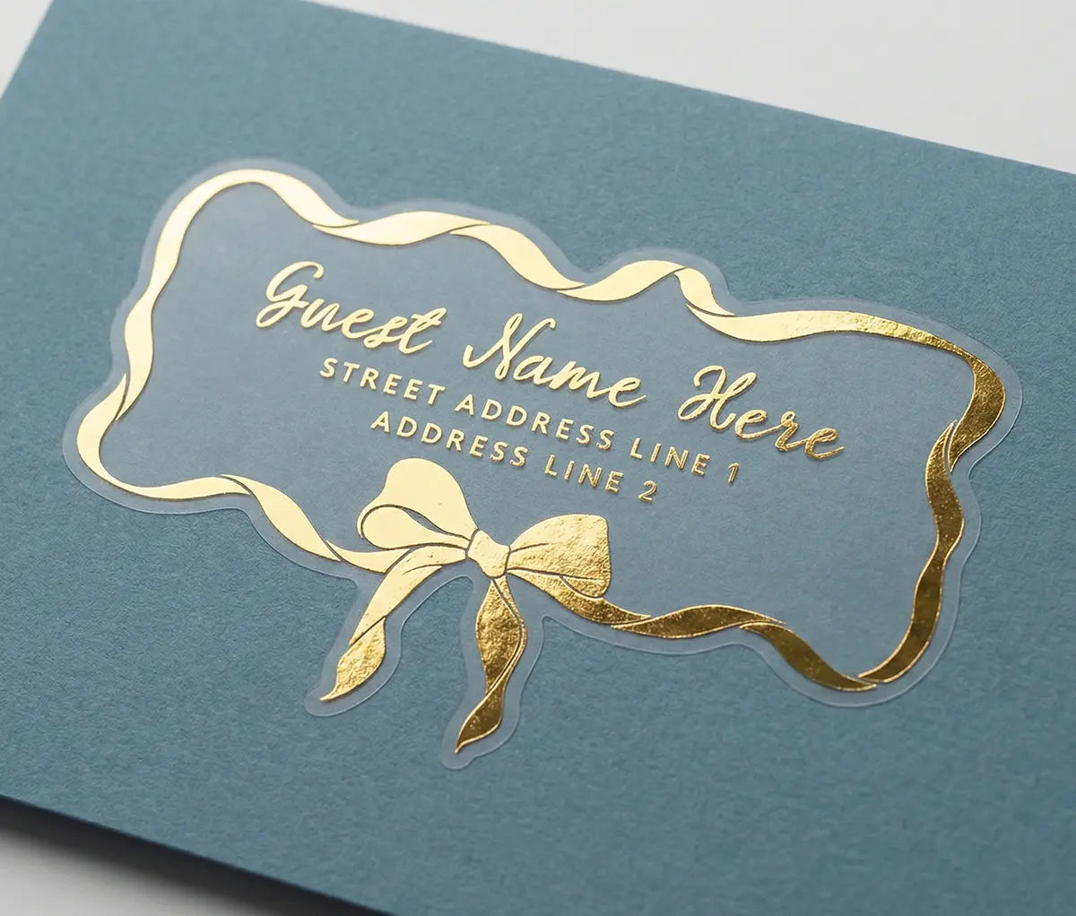 Guest address label printed in gold foil applied to a blue colour envelope with custom die-cut whimsical bow and ribbon shape.
